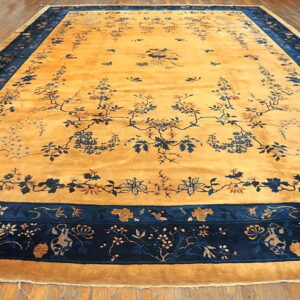 A large saffron rug with a navy blue floral border and detailed vine motifs rests on wood plank flooring.