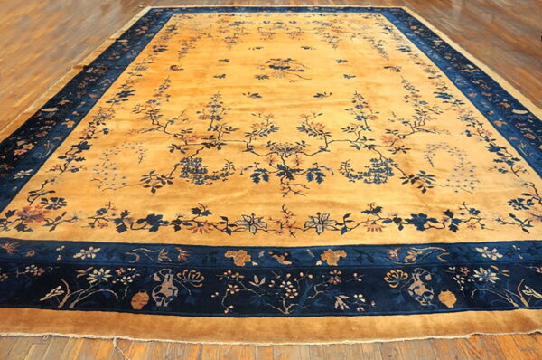 A large saffron rug with a navy blue floral border and detailed vine motifs rests on wood plank flooring.