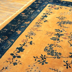 Mustard yellow rug featuring a dark blue floral border and scattered botanical motifs resting on light hardwood.