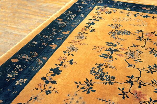 Mustard yellow rug featuring a dark blue floral border and scattered botanical motifs resting on light hardwood.