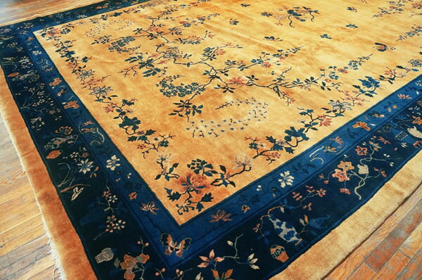 Golden high-pile rug with a sprawling floral pattern and a wide dark blue patterned border on wood floors.