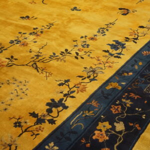Yellow medium-pile rug with sprawling floral vines and a wide, dark navy pictorial border on wood floor.