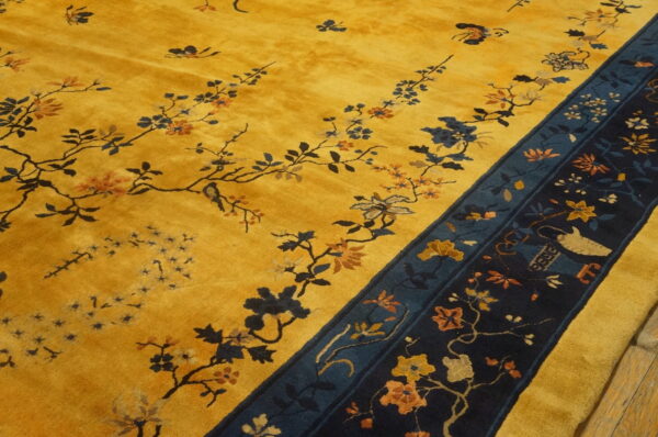 Yellow medium-pile rug with sprawling floral vines and a wide, dark navy pictorial border on wood floor.