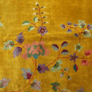 Detail of a shiny gold rug with stylized purple, pink, and green flowers and leaves.