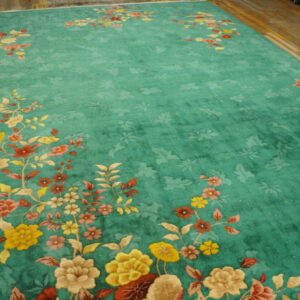 Teal area rug with gold and red sprawling floral motifs laid out on rustic wood flooring.