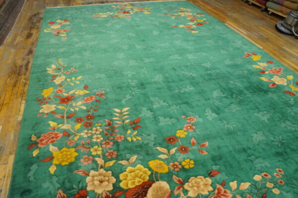 Teal area rug with gold and red sprawling floral motifs laid out on rustic wood flooring.