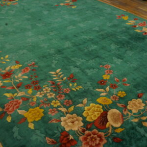 Teal high-pile rug with subtle field carving and elaborate colorful floral border on a wood floor.