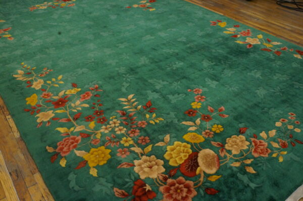 Teal high-pile rug with subtle field carving and elaborate colorful floral border on a wood floor.