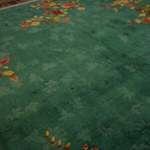 Teal green rug with carved floral pattern and bright yellow and red sprays on wood floor.