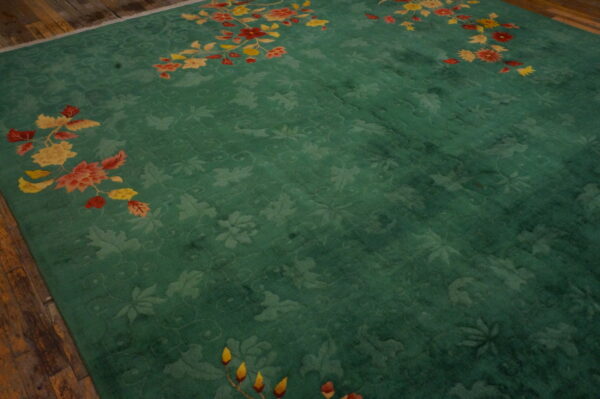 Teal green rug with carved floral pattern and bright yellow and red sprays on wood floor.