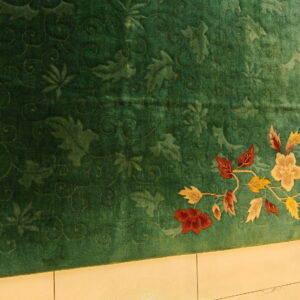 Green carved rug featuring a tone-on-tone background and a multi-color floral vine border on tile.