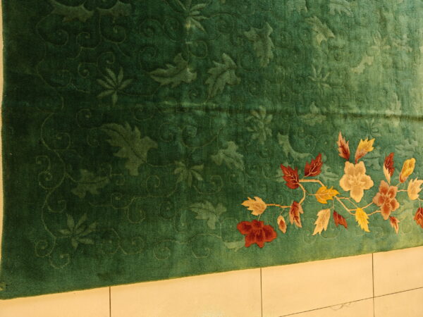 Green carved rug featuring a tone-on-tone background and a multi-color floral vine border on tile.