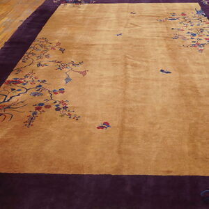 Tan area rug featuring scattered multicolored floral designs and a wide, solid deep purple border on wood flooring.