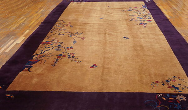 Tan area rug featuring scattered multicolored floral designs and a wide, solid deep purple border on wood flooring.