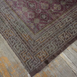 A distressed purple and gray rug with a geometric border rests on rustic gray wood flooring.
