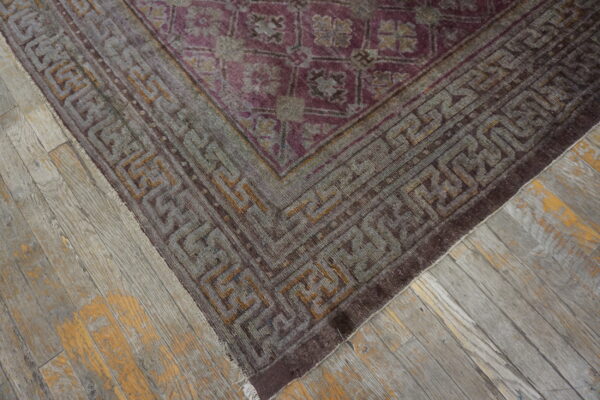 A distressed purple and gray rug with a geometric border rests on rustic gray wood flooring.