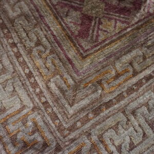 High pile rug detail showing complex geometric borders and field patterns in brown, gray, and purple tones.