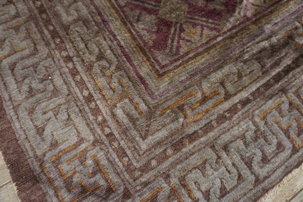 High pile rug detail showing complex geometric borders and field patterns in brown, gray, and purple tones.