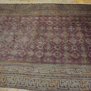 Purple and gray rug with a repeating trellis motif and wide geometric borders on light wood flooring.
