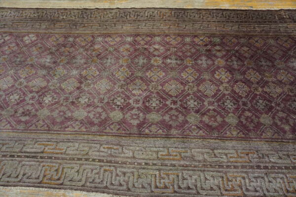Purple and gray rug with a repeating trellis motif and wide geometric borders on light wood flooring.