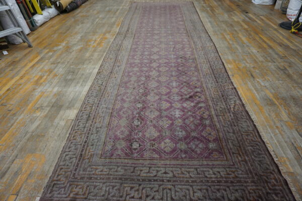 A long, low-pile mauve runner rug with geometric patterns rests on distressed wood flooring.