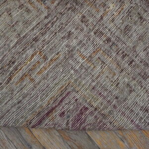 The tightly woven back of a rug shows geometric patterns in gray, brown, and maroon threads on wooden floorboards.