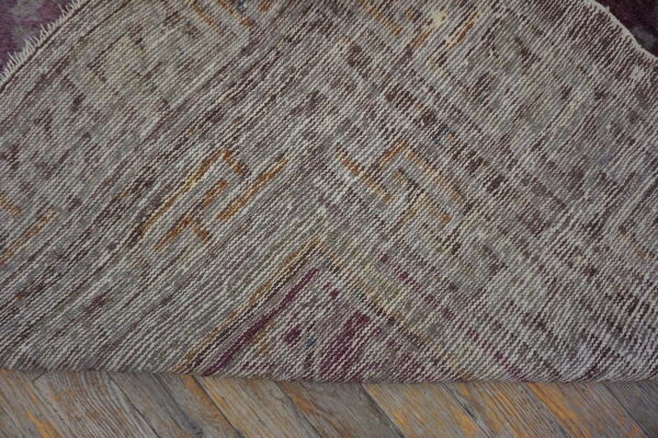 The tightly woven back of a rug shows geometric patterns in gray, brown, and maroon threads on wooden floorboards.
