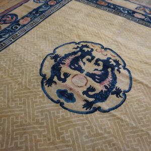 Tan rug with a maze pattern, blue dragon medallion, and complex floral borders on wooden floorboards.