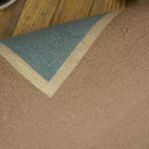 Rolled-back low-pile rug corner displaying tan, cream, and teal stripes on rustic wood floor.