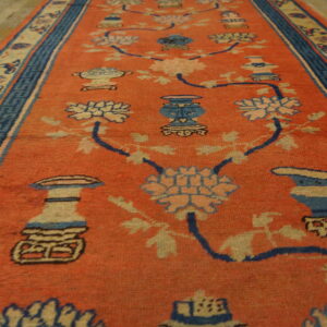 Rusty orange runner rug displays a pattern of blue vases and florals on light wood flooring.