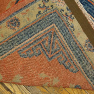 Terracotta and blue geometric border rug corner folded over distressed wood flooring.