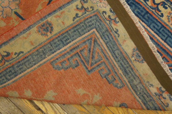 Terracotta and blue geometric border rug corner folded over distressed wood flooring.