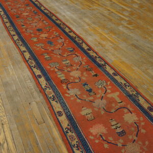 Rust runner with blue and tan floral and vase patterns displayed on aged wood floorboards.