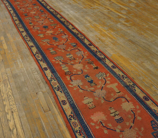 Rust runner with blue and tan floral and vase patterns displayed on aged wood floorboards.