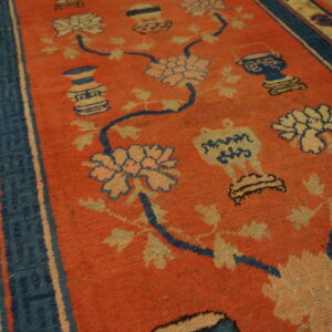 Orange rug featuring a sprawling pattern of cream flowers and blue vases, bordered by navy stripes.