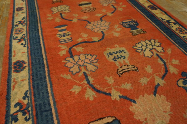 Orange rug featuring a sprawling pattern of cream flowers and blue vases, bordered by navy stripes.
