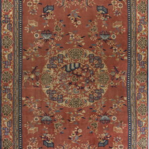 Red-orange rug featuring dense patterns of stylized flowers and vines outlined by blue borders.