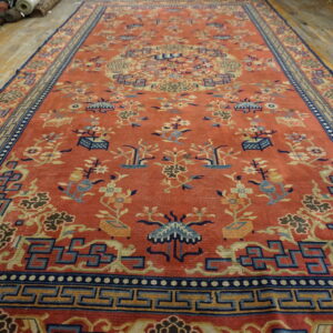 Long rust-colored rug with blue and yellow floral patterns and geometric borders on wood flooring.