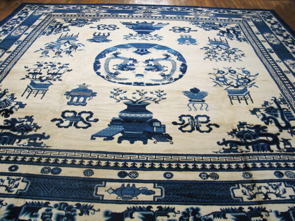 Ivory rug with indigo blue pictorial patterns of dragons and urns, framed by detailed borders on wood floor.