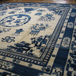 Large cream rug featuring a rich indigo Chinese scenic and medallion pattern on wood flooring.