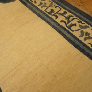 Low-pile gold rug featuring a navy and slate floral border, partially visible on wood flooring.