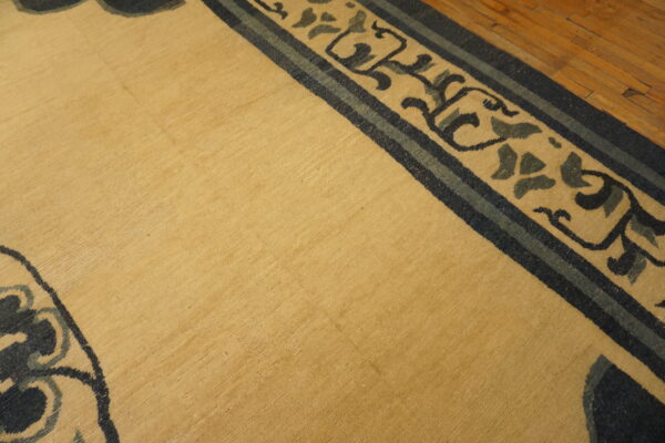Low-pile gold rug featuring a navy and slate floral border, partially visible on wood flooring.