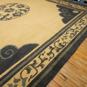 Beige rug featuring a detailed border pattern of navy blue scrolls and dusty green accents on wood flooring.