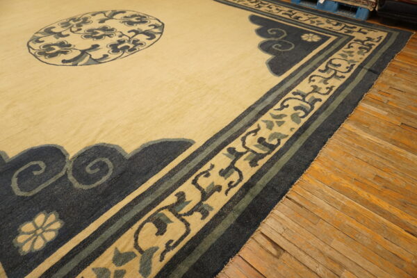 Beige rug featuring a detailed border pattern of navy blue scrolls and dusty green accents on wood flooring.
