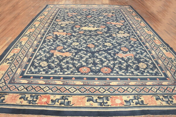 Navy blue rug with a coral and cream animal and floral pattern resting on a polished wood floor.