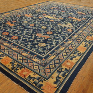 Navy blue rug with complex gold and orange floral and animal patterns lies angled on hardwood floors.