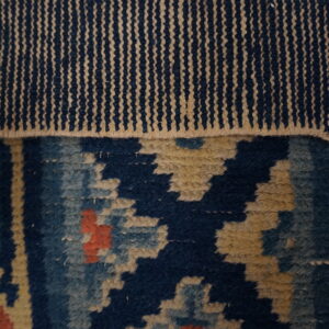 The rug shows a flat woven navy and tan striped edge above a geometric navy and coral pile.