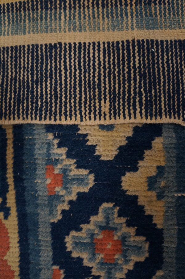 The rug shows a flat woven navy and tan striped edge above a geometric navy and coral pile.