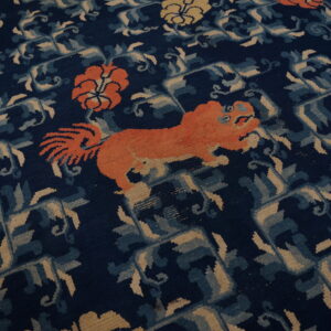 Navy rug with an orange animal and floral motifs set against blue and tan interlocking geometric designs.