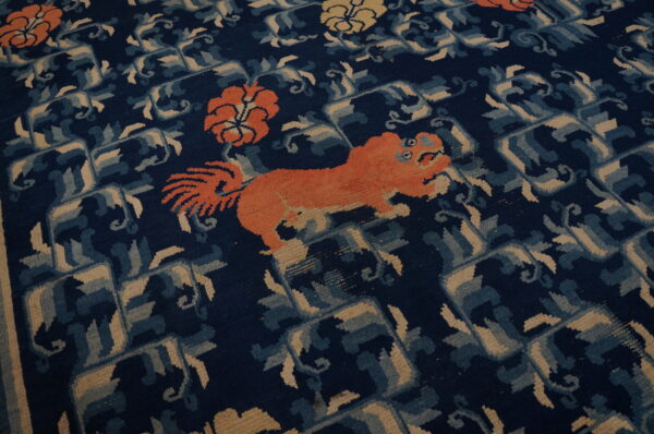 Navy rug with an orange animal and floral motifs set against blue and tan interlocking geometric designs.